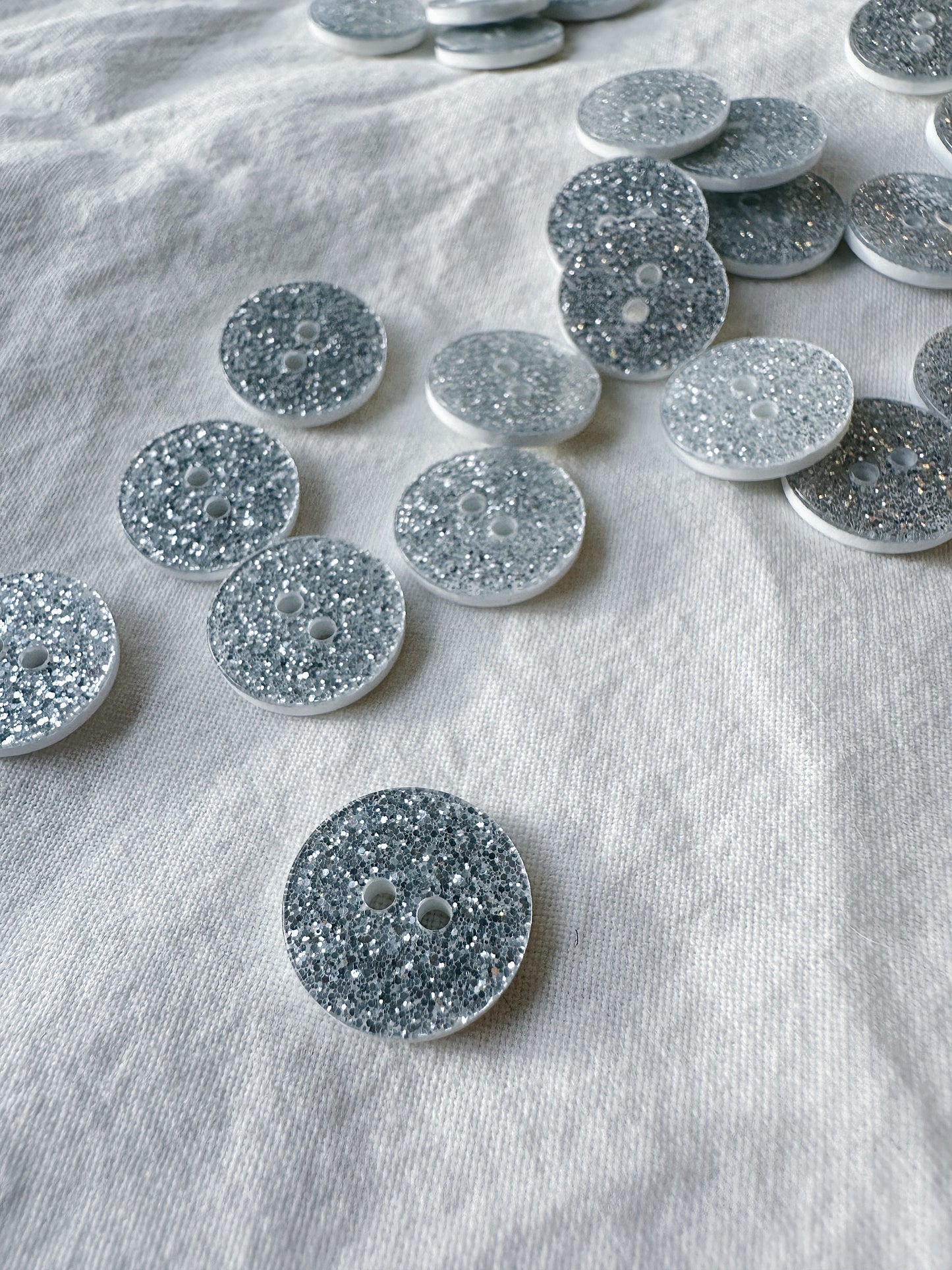Kuvassa on hopeita glitter nappeja (buttons) vaatteisiin.