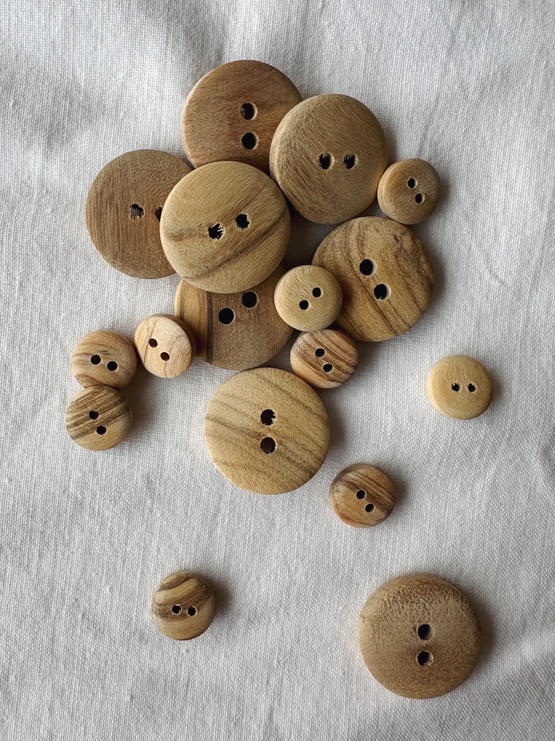 Kuvassa on eri kokoisia oliivipuisia nappeja (buttons). 