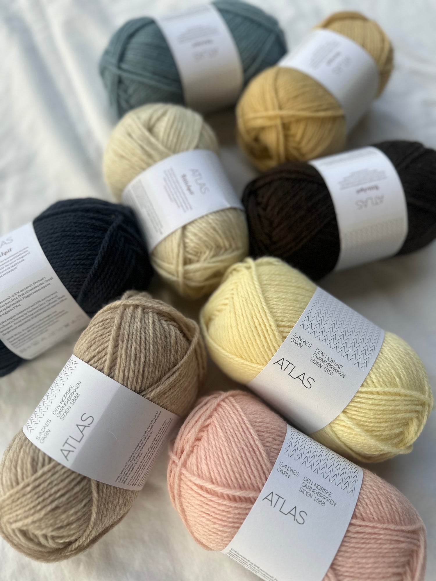 Kuvassa on Sandnes Garn Atlas -lankoja levitettynä valkoisen lakanan päälle.